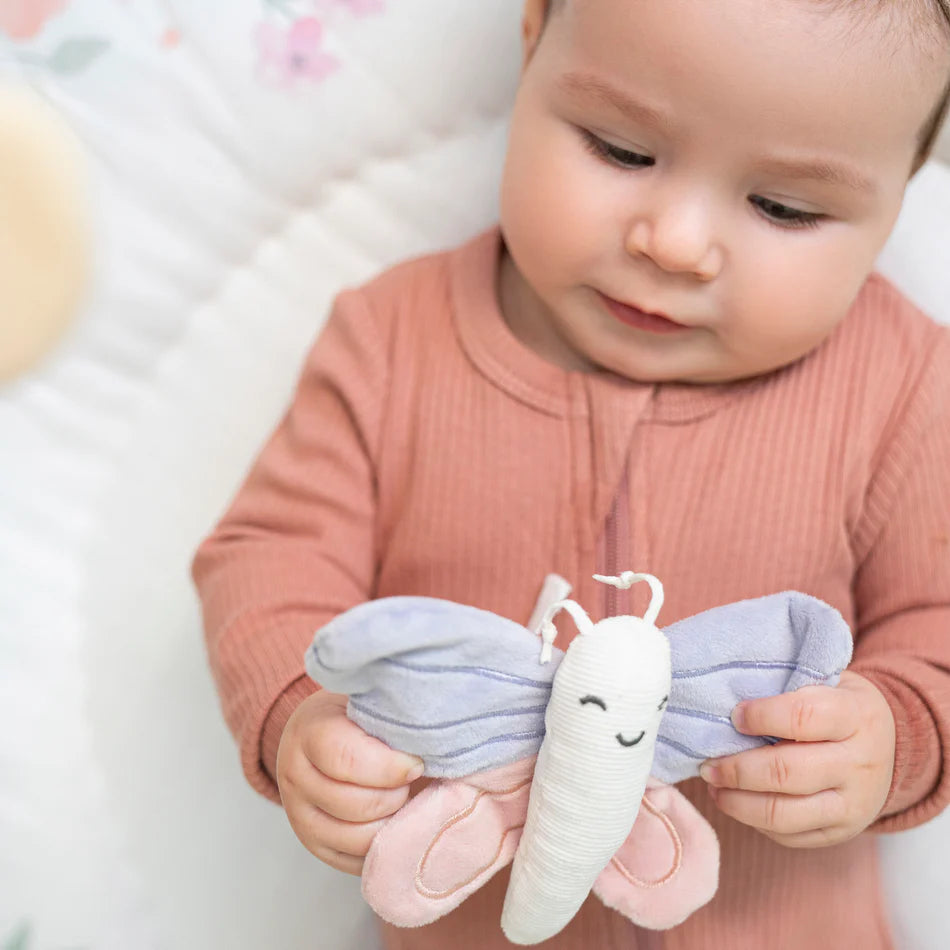 Baby holding a soft fabric butterfly toy while sitting on the Ma Fleur Activity Gym, showcasing its gentle colors and interactive play features.