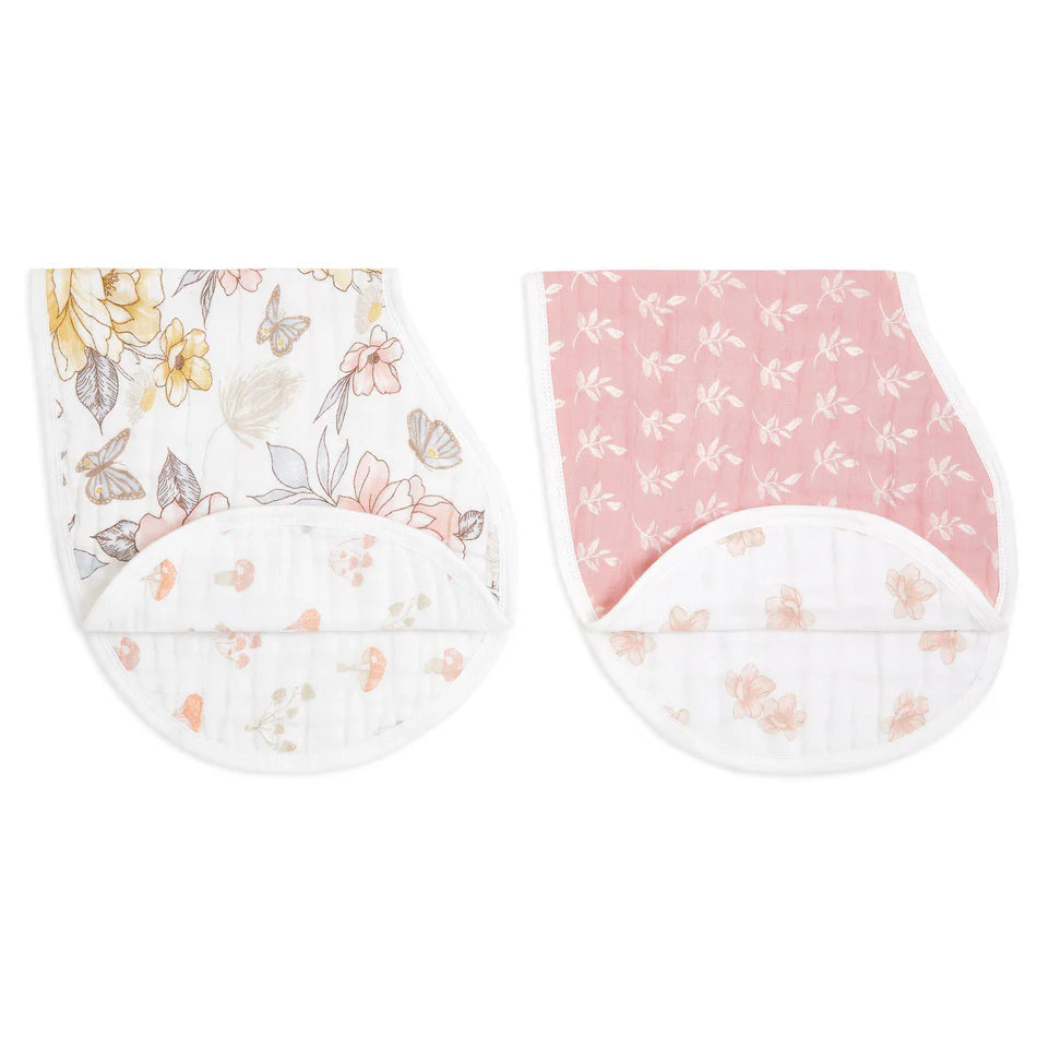 Earthly 2-pack Organic Burpy Bibs featuring a floral print in soft yellow and gray tones paired with a pink bib adorned with delicate leaves, both made from breathable organic muslin fabric.