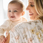 Smiling mother holding her happy baby wearing Earthly 2-pack Organic Burpy Bibs with a soft floral and butterfly pattern, showcasing gentle and natural baby essentials.
