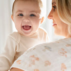 Smiling baby resting on mother's shoulder wearing an Earthly 2-pack Organic Burpy Bibs soft muslin burp cloth with subtle animal and floral prints, ideal for baby feeding and newborn essentials.