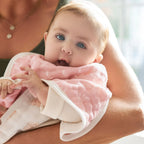 Baby wearing a pink muslin bib being held by an adult, showcasing the Earthly 2-pack Organic Burpy Bibs designed for comfort and practicality during feeding time.
