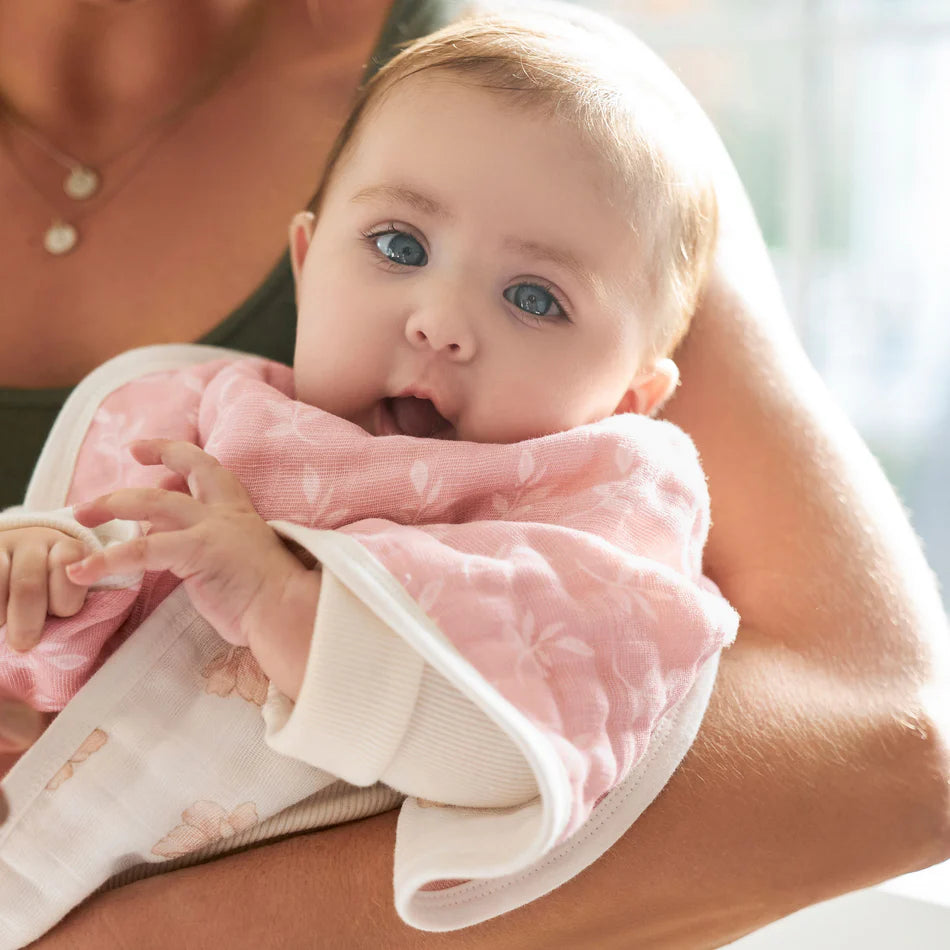 Baby wearing a pink muslin bib being held by an adult, showcasing the Earthly 2-pack Organic Burpy Bibs designed for comfort and practicality during feeding time.