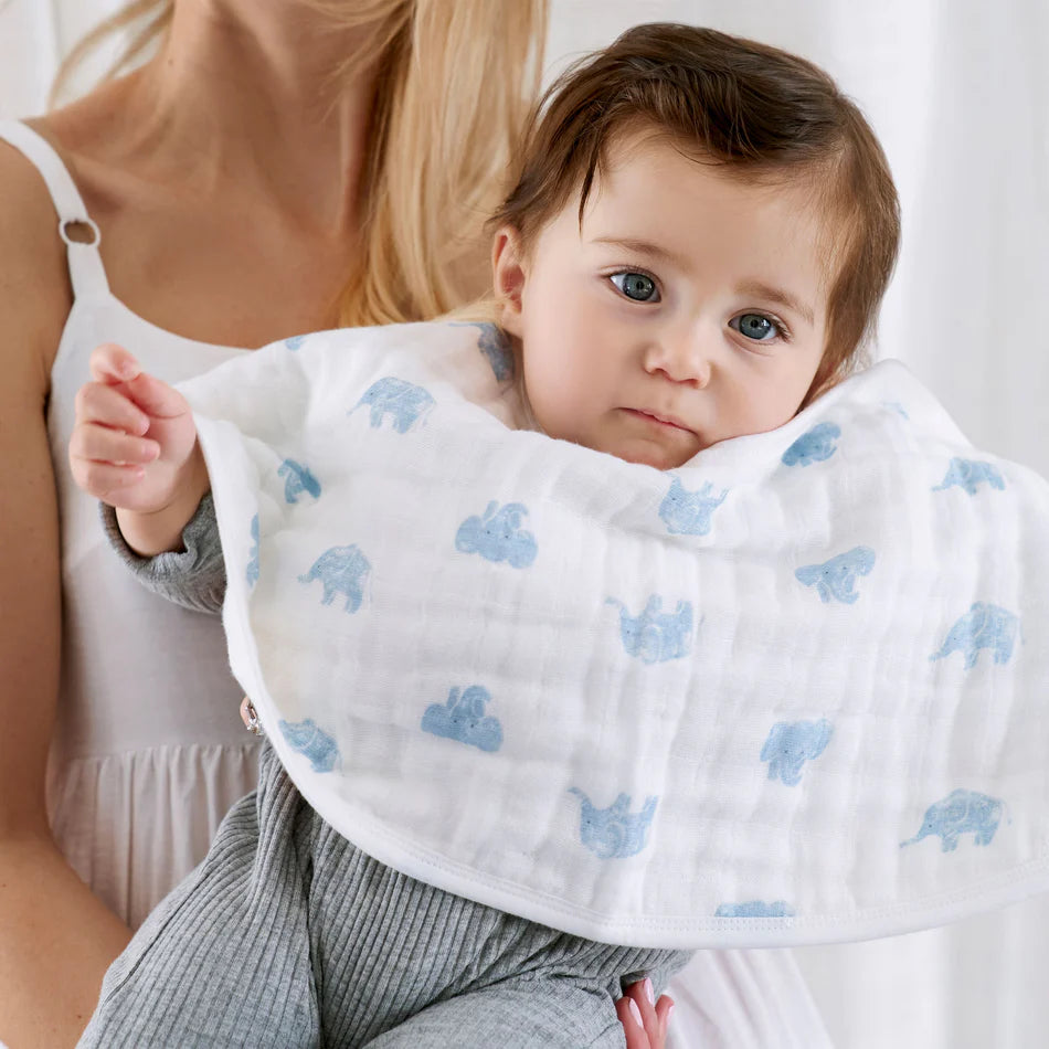 Baby wearing Animal Kingdom 2-pack Burpy Bibs featuring soft, organic muslin fabric with light blue animal prints, held by a woman in a white tank top.