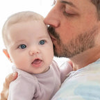 Father gently kissing baby wearing Above the Clouds 2-Pack Organic Burpy Bibs in a soft, natural setting, highlighting comfort and care for newborn essentials.